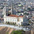 Vista aérea do Santuário de Nossa Senhora da Penha, localizado no alto de um penhasco na Zona Norte do Rio de Janeiro, com a paisagem urbana densa ao fundo.
